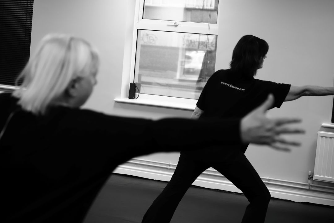 two dancers with backs to camera reaching to the side