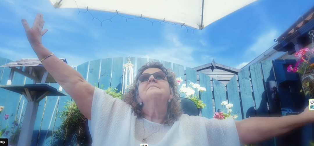 female dancer sitting in a chair in the garden reaching with both arms under a blue sky