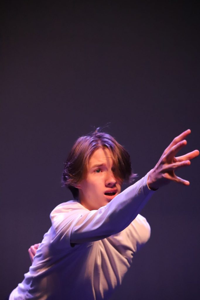 Young male dancer performing on stage reaching forward with right arm
